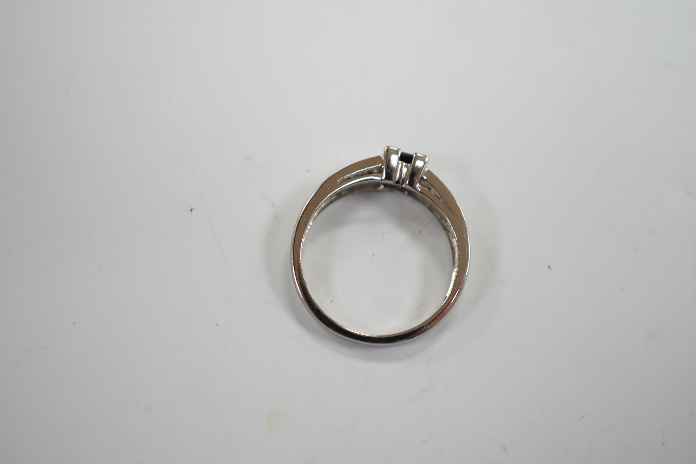 A modern 18ct white gold and single stone square cut sapphire set ring, with baguette cut diamond set shoulders, size N, gross weight 2.9 grams.
